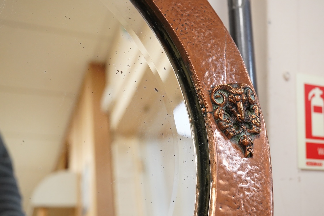 An oval late 19th century hammered copper wall mirror with rams head cartouches, 65cm wide